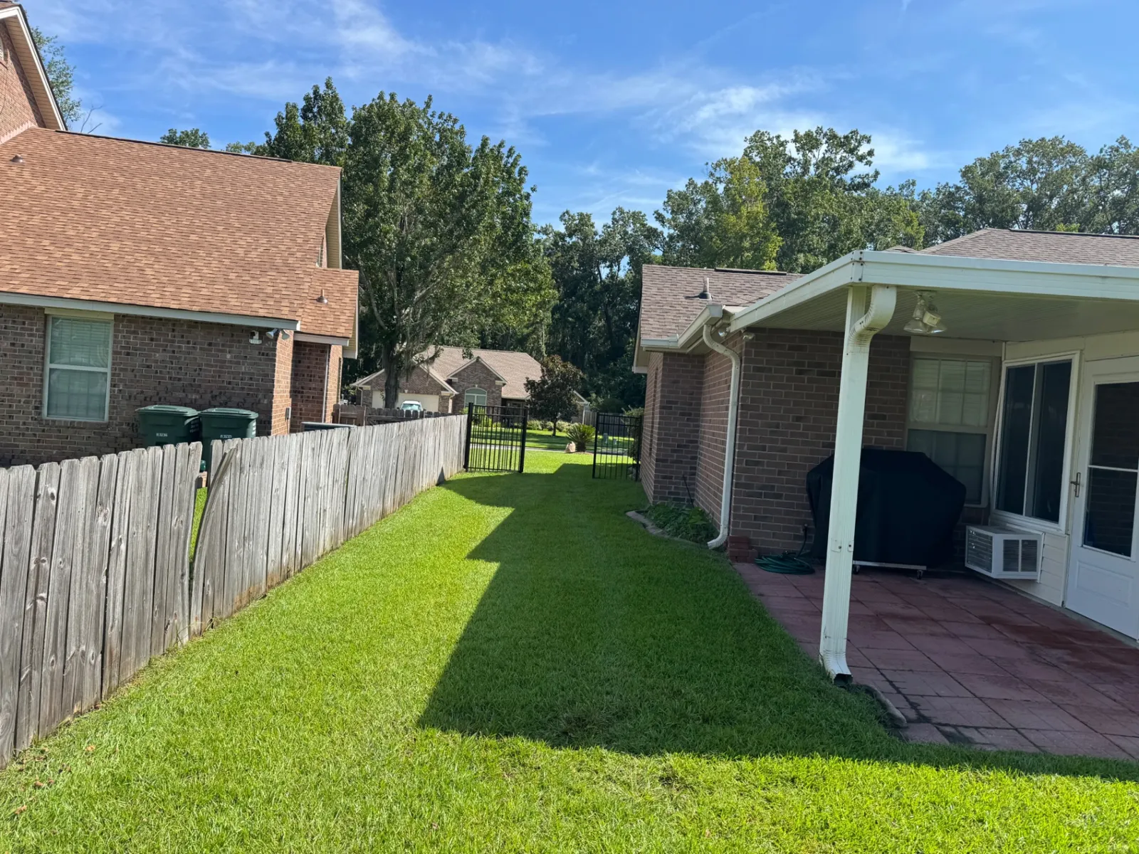 Side yard with healthy trimmed turf between a wood privacy fence and a covered brick patio